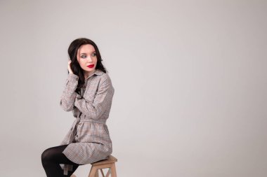 Beyaz tenli, seksi, profesyonel bir model. Stüdyoda, sandalyede oturan, beyaz arka planda izole bir şekilde poz veriyor. Boşluğu kopyala.