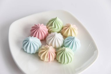 Beyaz arka planda renkli kurabiyelerle dolu bir tabak.