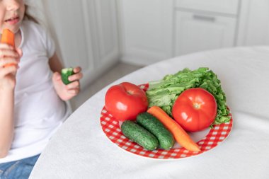 Küçük kız mutfakta sebze yiyor. Sağlıklı yemek. Vejetaryenlik. Çocuk bitki yiyor.