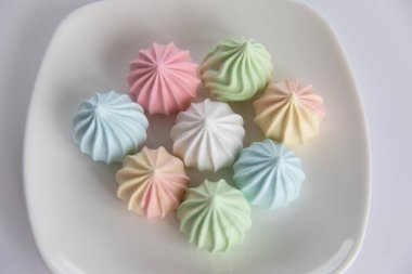 Beyaz arka planda renkli kurabiyelerle dolu bir tabak.