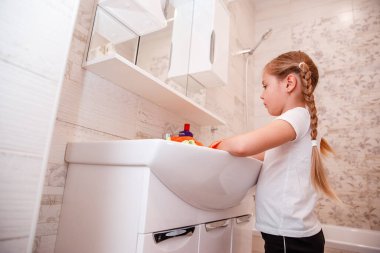 Çocuk lavaboda ellerini yıkıyor. Küçük kız lavaboyu ve musluğu yıkıyor.