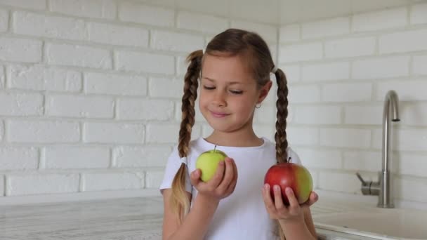 En liten flicka med äpplen i köket. Barn biter äter ett äpple — Stockvideo