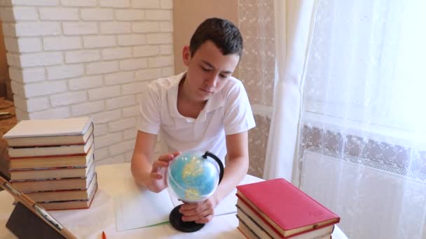 Der Teenie-Junge schreibt Blicke auf die Weltkugel. Student studiert Geografie — Stockvideo