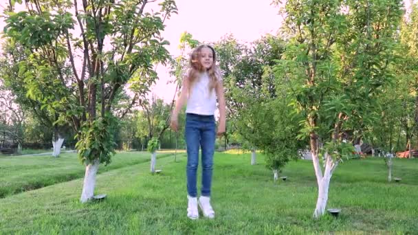 Маленька Дівчинка Довгим Волоссям Джинсах Стрибає Маленька Дівчинка Зеленому Саду — стокове відео