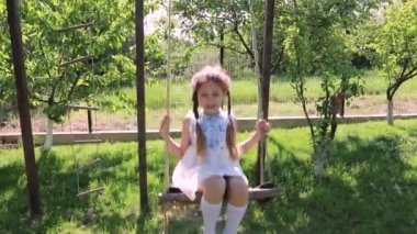 Küçük kız sallanıyor. Yeşil bahçedeki küçük tatlı kız sallanıyor salıncakta