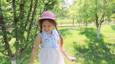 Yeşil bir yaz bahçesinde, elbise giymiş, şapkalı şirin bir kız gülüyor. Bebek gülüşü, gülümseme. Çocuğun mutluluğu.