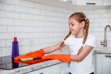 Temizlik. Küçük kız güzel mutfakta mutfak sobasını temizliyor.