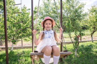 Küçük kız sallanıyor. Yeşil bahçedeki küçük tatlı kız sallanıyor salıncakta