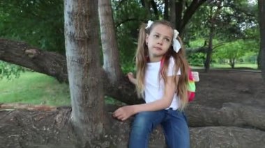 Sırt çantalı tatlı bir kız ağaca tırmanıyor. Yeşil parktaki bir çocuk..