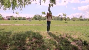 Çocuk söğüt ağacının dallarına biniyor. Yeşil parktaki küçük kız