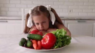 Küçük kız sebze yemek istemiyor. Çocuk sinirlenir ve arkasını döner. Mutfaktaki küçük kız sağlıklı yemek yemek istemiyor.