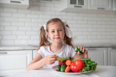 Küçük kız mutfakta sebze yiyor. Sağlıklı yemek. - Evet. Çocuk bitki yiyeceği yiyor. Boşluğu kopyala