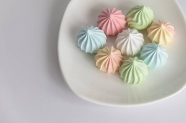 Beyaz arka planda renkli kurabiyelerle dolu bir tabak.