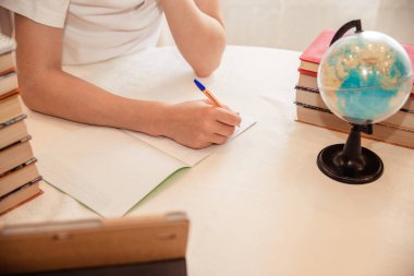 Genç bir çocuk ev ödevini yapıyor. Ders kitapları ve defterler masanın üzerinde.