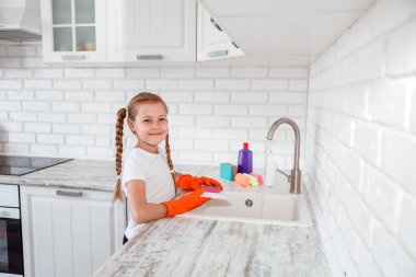 Beyaz tişörtlü kız mutfakta bulaşıkları yıkıyor. Çocuklar için ev işleri