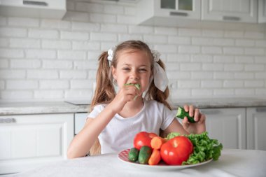 Küçük kız mutfakta sebze yiyor. Sağlıklı yemek. Vejetaryenlik. Çocuk bitki yiyor.
