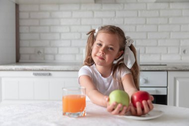 Mutfakta meyve suyu ve elma suyu olan küçük bir kız. Sağlıklı yemek. Vejetaryenlik. Vitaminler. Boşluğu kopyala