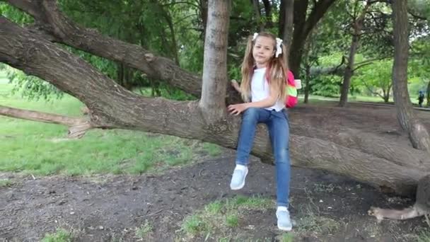 Una niña sentada en un árbol. un niño en un parque verde. — Vídeo de stock