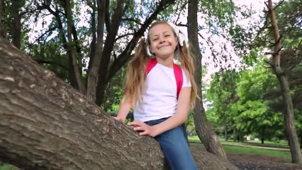 Маленькая девочка сидит на дереве. ребенок в зеленом парке. — стоковое видео