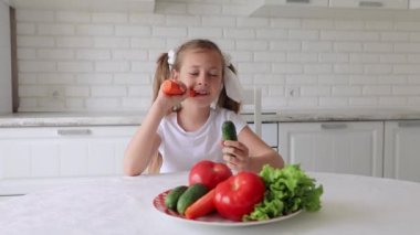 Çocuk neşe ve zevkle sebze yer. Küçük bir kız mutfakta yemek yiyor..