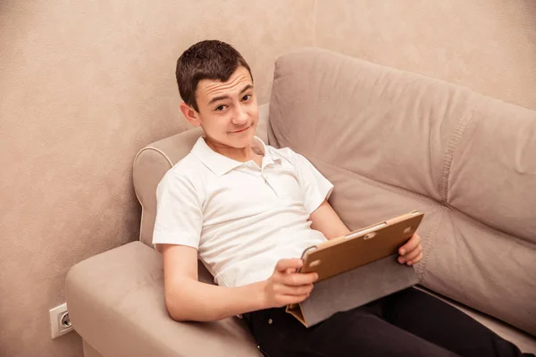 白いTシャツを着た10代の男の子がラップトップでソファに座っています 家庭教育子供の自己教育 — ストック写真