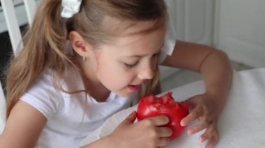 Mutfak masasında oturmuş organik sebzeler yiyen, olgun kırmızı domates yiyen komik küçük kız..