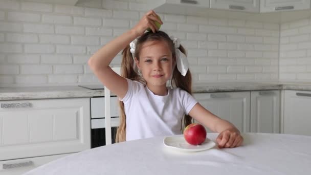 Uma menina põe uma maçã na cabeça. criança segura uma maçã na cabeça. — Vídeo de Stock