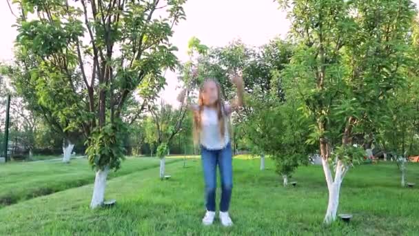 Маленька дівчинка з довгим волоссям в джинсах стрибає. маленька дівчинка в зеленому саду. дитяче щастя — стокове відео