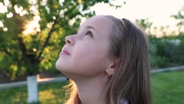 Malá roztomilá holčička se dívá do nebe v dálce. západ slunce. Léto. Park, zahrada. velký portrét dítěte,. — Stock video