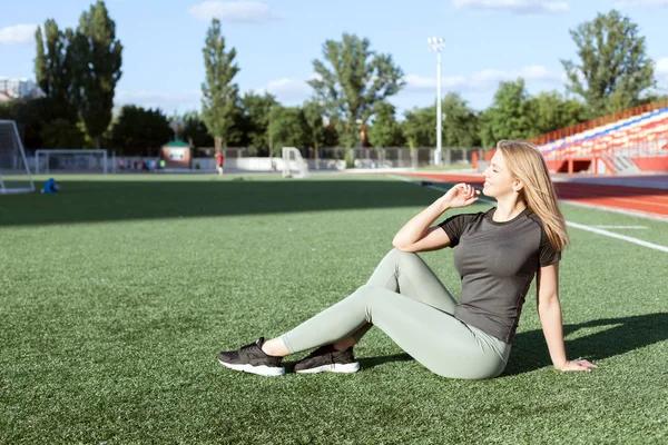 スポーツウェアの若い女性がスタジアムでサッカーのフィールドで座っています — ストック写真