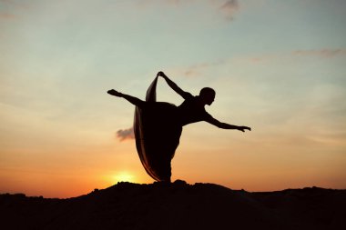 Günbatımı güneş, çölde bir dans eden kadın silüeti.