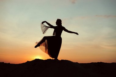 Gün batımında, dans hareketleri o yapar çölde bir kadın silüeti.