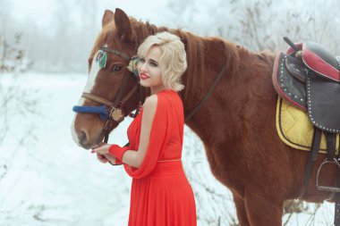 Bir at kış ormandaki yakınındaki Kırmızı elbiseli sarışın bir kadın portresi.