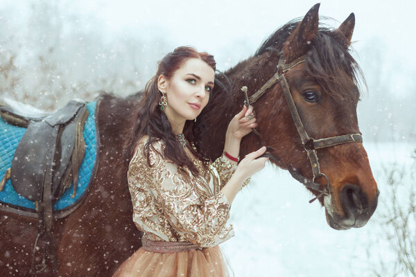 Beautiful young woman stands near the horse. They are in a winter park.