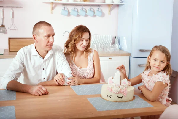 Dad, mom and daughter are sitting in the kitchen at the table.