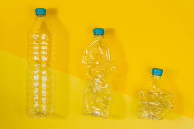 Sarı arka planda şeffaf ve ezilmiş plastik şişelerin olduğu yatay renk görüntüsü. Geri dönüşüm ve çevre kavramı.
