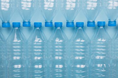 Mavi arka planda üst üste istiflenmiş boş, şeffaf plastik şişelerin ön görüntüsüyle yatay renk görüntüsü. Geri dönüşüm ve çevre kavramı.
