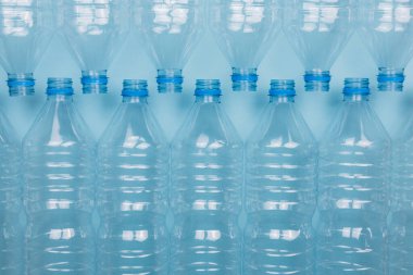 Mavi arka planda kapağı olmayan boş, şeffaf plastik şişelerin ön görüntüsüyle yatay renk görüntüsü. Geri dönüşüm ve çevre kavramı.