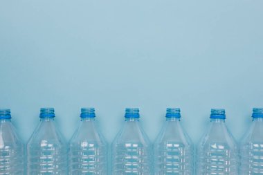 Mavi arka planda kapağı olmayan boş, şeffaf plastik şişelerin ön görüntüsüyle yatay renk görüntüsü. Geri dönüşüm ve çevre kavramı.