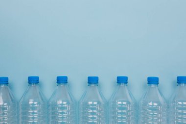Mavi arka planda üst üste istiflenmiş boş, şeffaf plastik şişelerin ön görüntüsüyle yatay renk görüntüsü. Geri dönüşüm ve çevre kavramı.