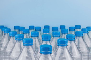 Mavi arka planda üst üste istiflenmiş boş, şeffaf plastik şişelerin ön görüntüsüyle yatay renk görüntüsü. Geri dönüşüm ve çevre kavramı.