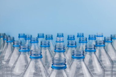 Mavi arka planda kapağı olmayan boş, şeffaf plastik şişelerin ön görüntüsüyle yatay renk görüntüsü. Geri dönüşüm ve çevre kavramı.