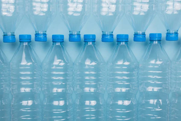 Mavi arka planda üst üste istiflenmiş boş, şeffaf plastik şişelerin ön görüntüsüyle yatay renk görüntüsü. Geri dönüşüm ve çevre kavramı.