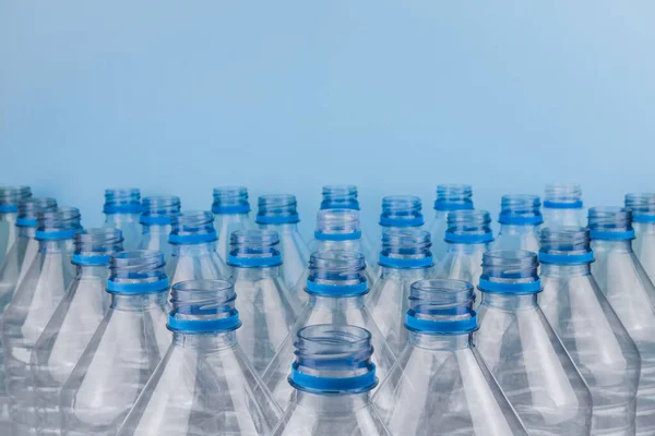 Horizontal color image with a front view of an empty clear plastic bottles without caps stacked on a blue background. Recycling and environment concept.