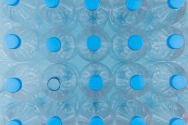 Mavi arka planda üst üste yığılmış boş, şeffaf plastik şişelerin olduğu yatay renk görüntüsü. Geri dönüşüm ve çevre kavramı.