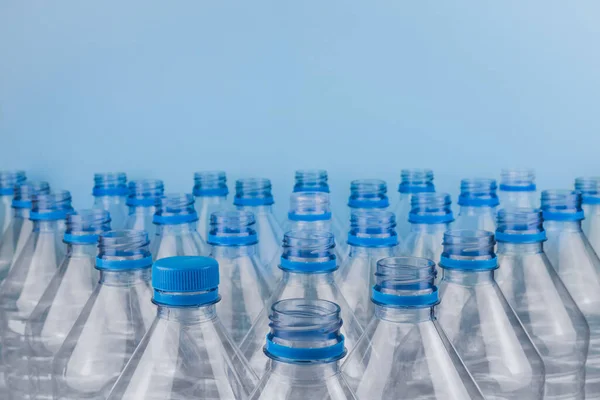 Horizontal color image with a front view of an empty clear plastic bottles with caps stacked on a blue background. Recycling and environment concept.