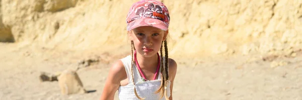 angry little six year old kid girl in a cap in nature in the desert. banner