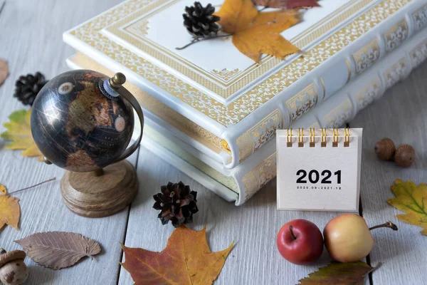 Calendar for 2021 and books, globe, colorful leaves on a light background. Cozy autumn composition.