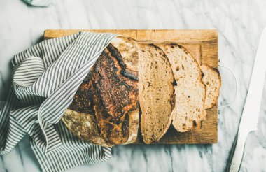 Fırından yeni çıkmış hamur mayası ekmek açık gri mermer renkli rustik Ahşap doğrama tahtası üzerinde parçalar halinde kesilmiş