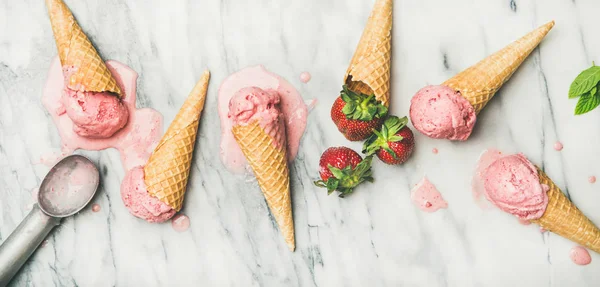 Healthy low calorie summer dessert. omemade yogurt ice cream with strawberries in waffle cones over grey marble background